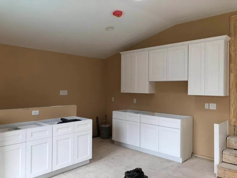 Unfinished kitchen with white cabinets against tan walls.