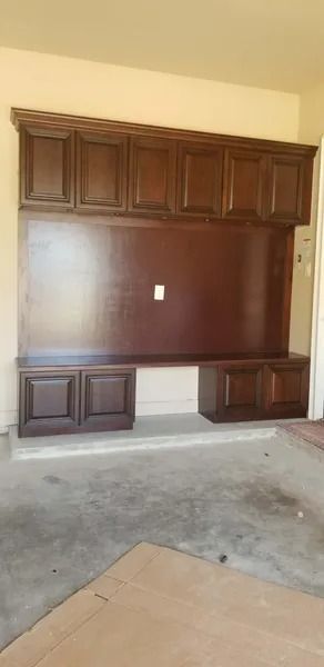 Dark wooden built-in entertainment center with upper cabinets, a large central panel, and lower cabinets against a concrete floor.