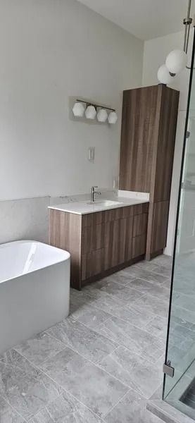 Modern bathroom with a bathtub, vanity, and a tall cabinet. Gray tile flooring.