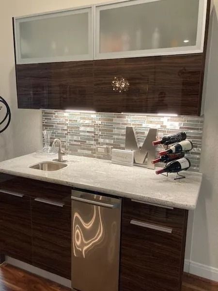 Modern wet bar with dark wood cabinets, stainless steel appliances, and white countertop.