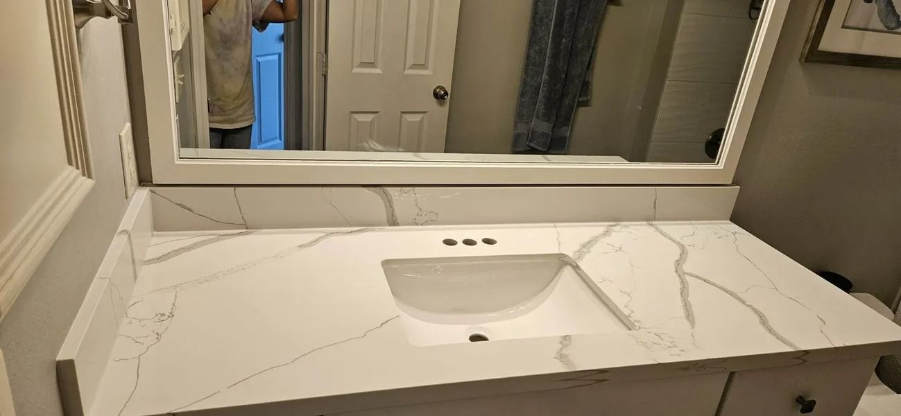 White bathroom vanity with a marble-like countertop, sink, and large mirror.