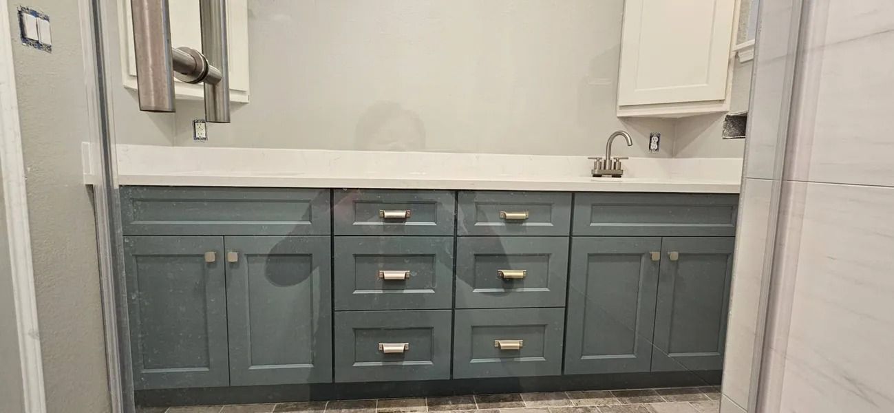 Bathroom vanity with gray-blue cabinets, white countertop, and silver faucet.