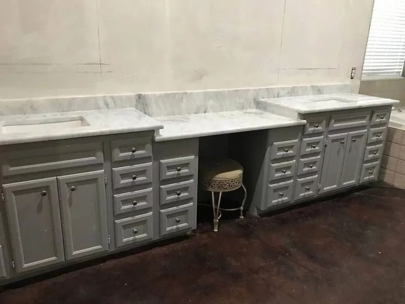 Bathroom with gray cabinets, marble countertops, and a vanity stool.