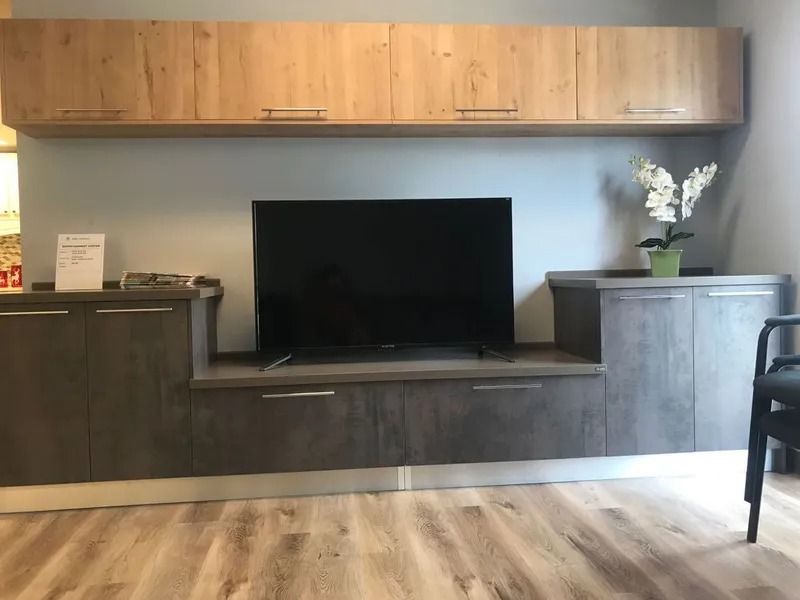 Entertainment center with a TV, cabinets, and overhead storage; wood tones.