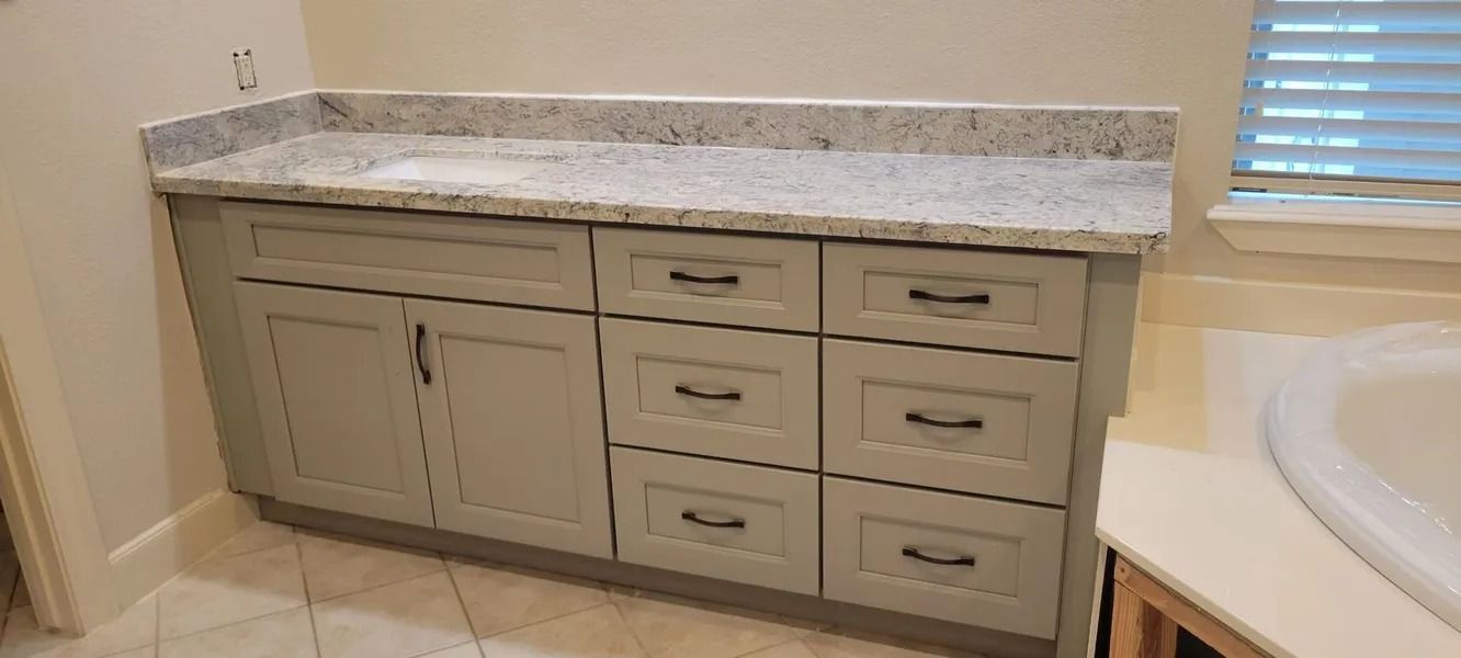 Bathroom vanity with light gray cabinets, granite countertop, and black hardware.