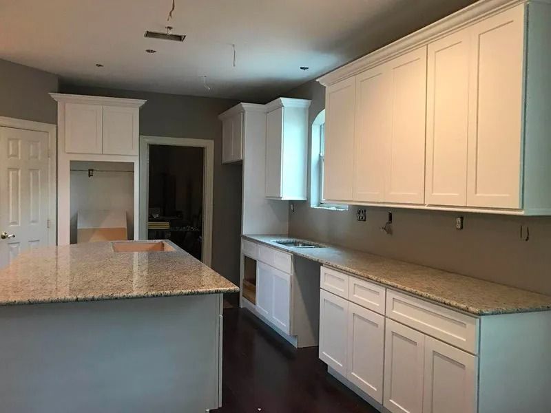 White kitchen cabinets with granite countertops, hardwood floors, and island.