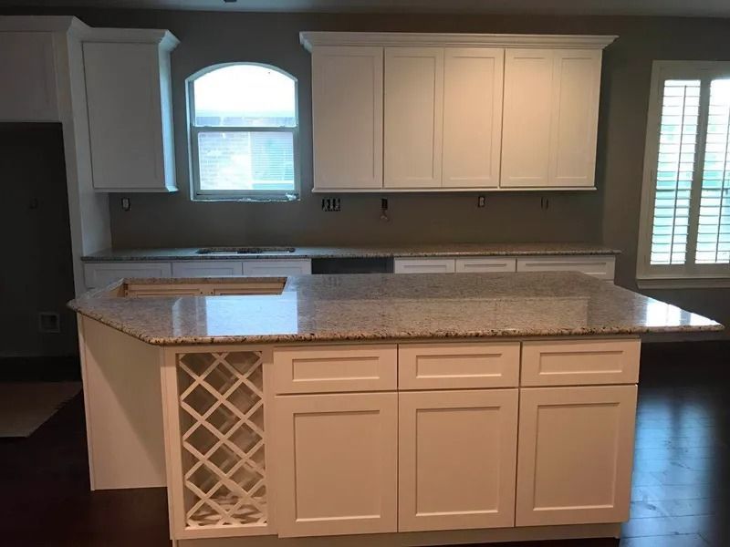 White kitchen with granite countertops, island with wine rack, and window.