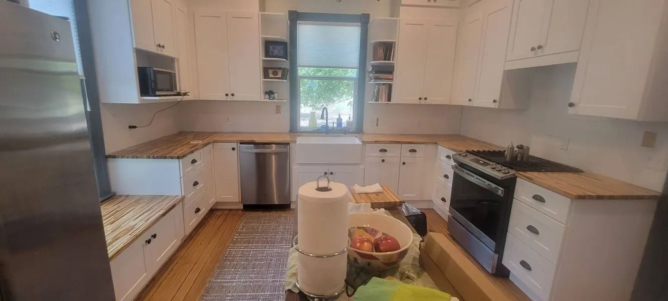 A bright, white kitchen with wood countertops and stainless steel appliances. A window is in the center.