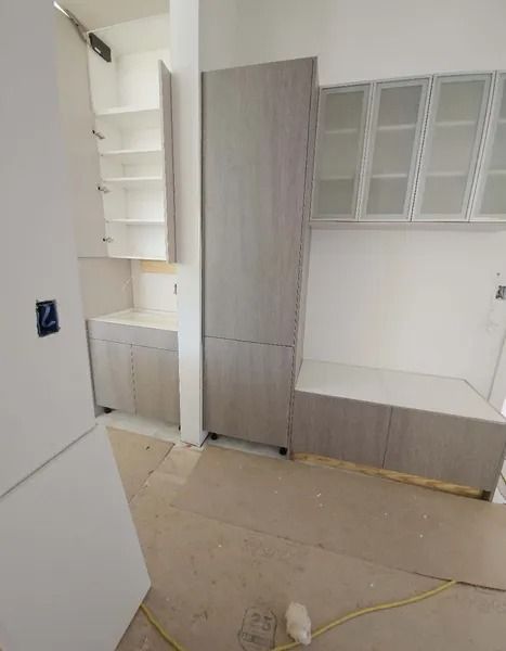 Kitchen cabinets being installed; tall cabinet, upper, lower, and glass-front cabinets are light wood-tone.
