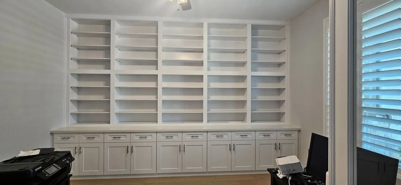 White built-in bookshelves with lower cabinets in a room with light-colored walls and blinds.