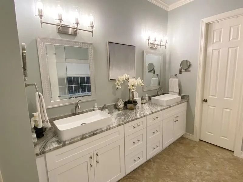 Bathroom with white cabinets, two sinks, mirrors, and light blue walls.