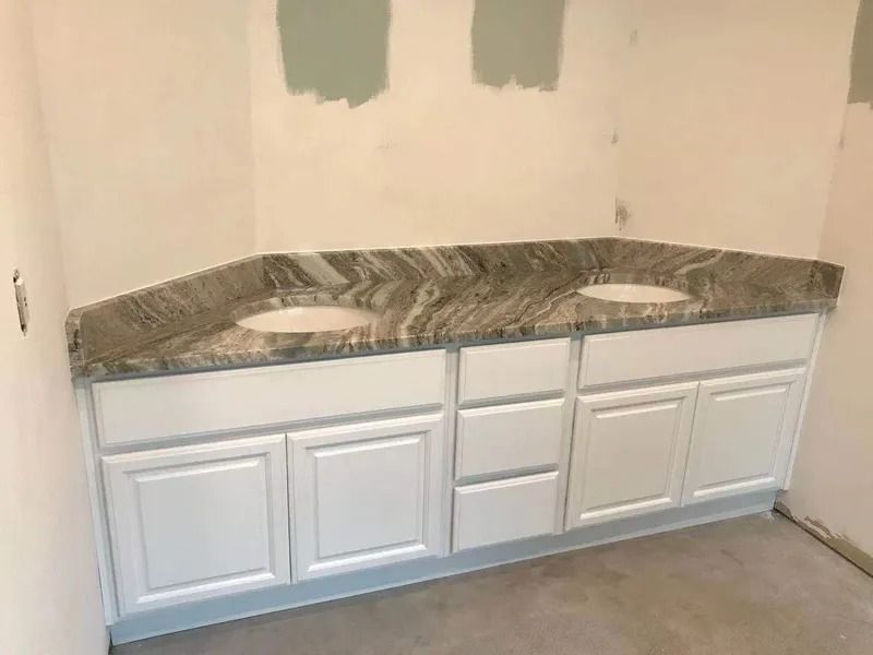 White bathroom vanity with granite countertop and two sinks, installed against a wall.