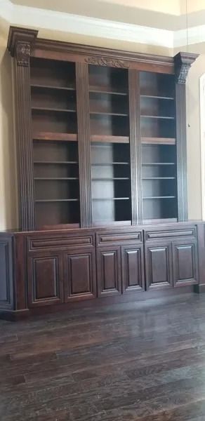 Dark wood built-in bookcase with open shelves above cabinet doors, set on wood floor.