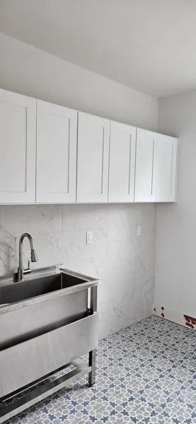 Laundry room with a stainless steel sink, white cabinets, patterned floor tiles, and a faucet.