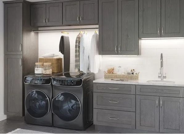 Gray laundry room with washer, dryer, cabinets, and a sink. Clothes hang on a rod.