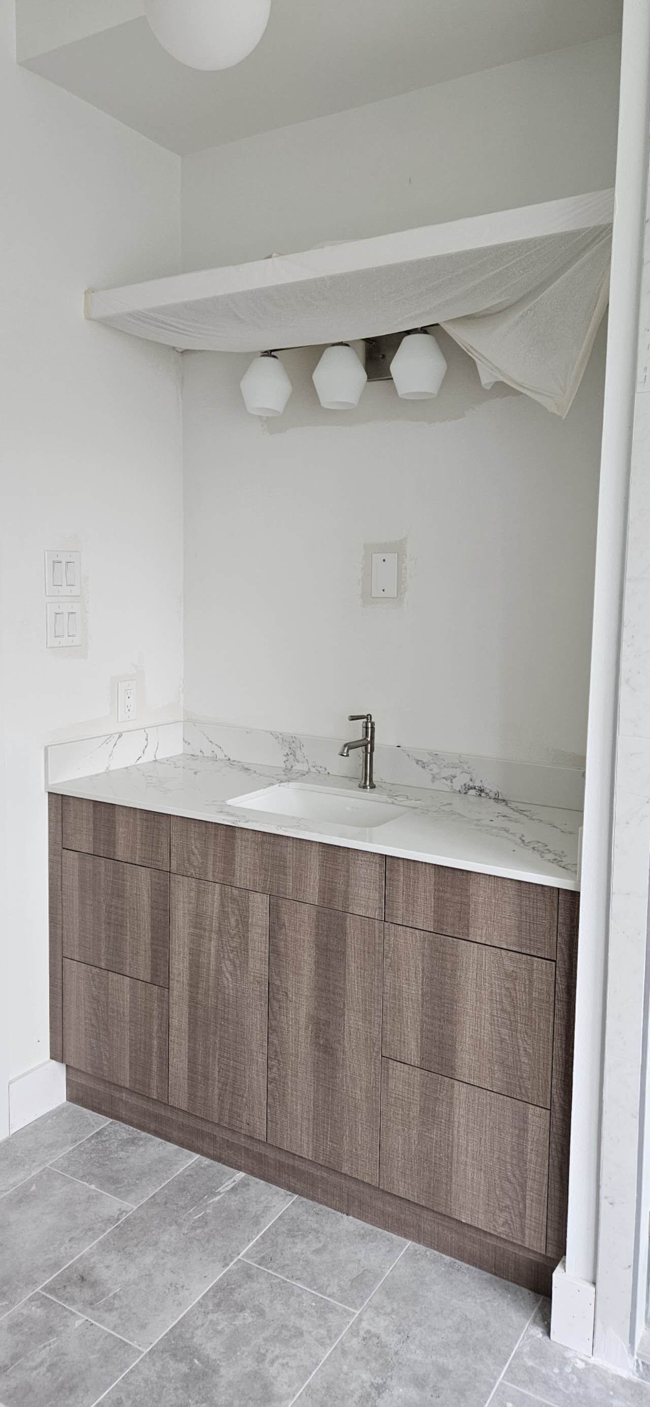 Bathroom vanity with a dark wood cabinet, white countertop, and three-light fixture. Gray tiled floor.