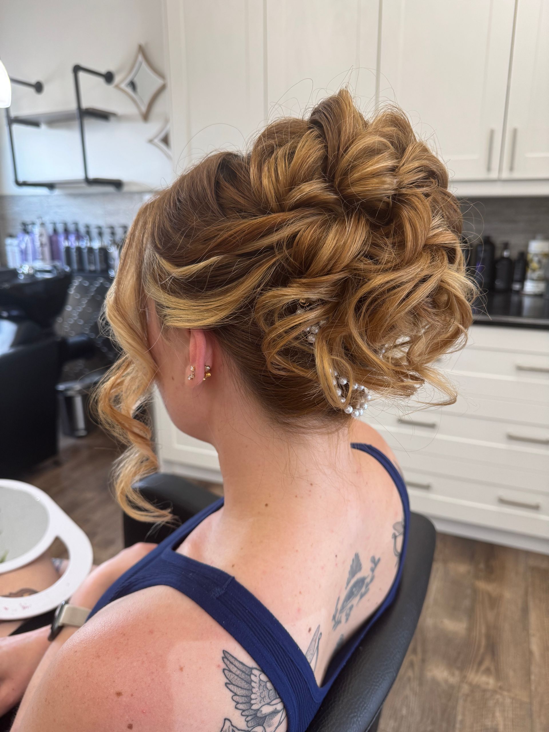 Woman with updo hairstyle, wearing a blue top, in a salon. Her hair is blonde with brown highlights.