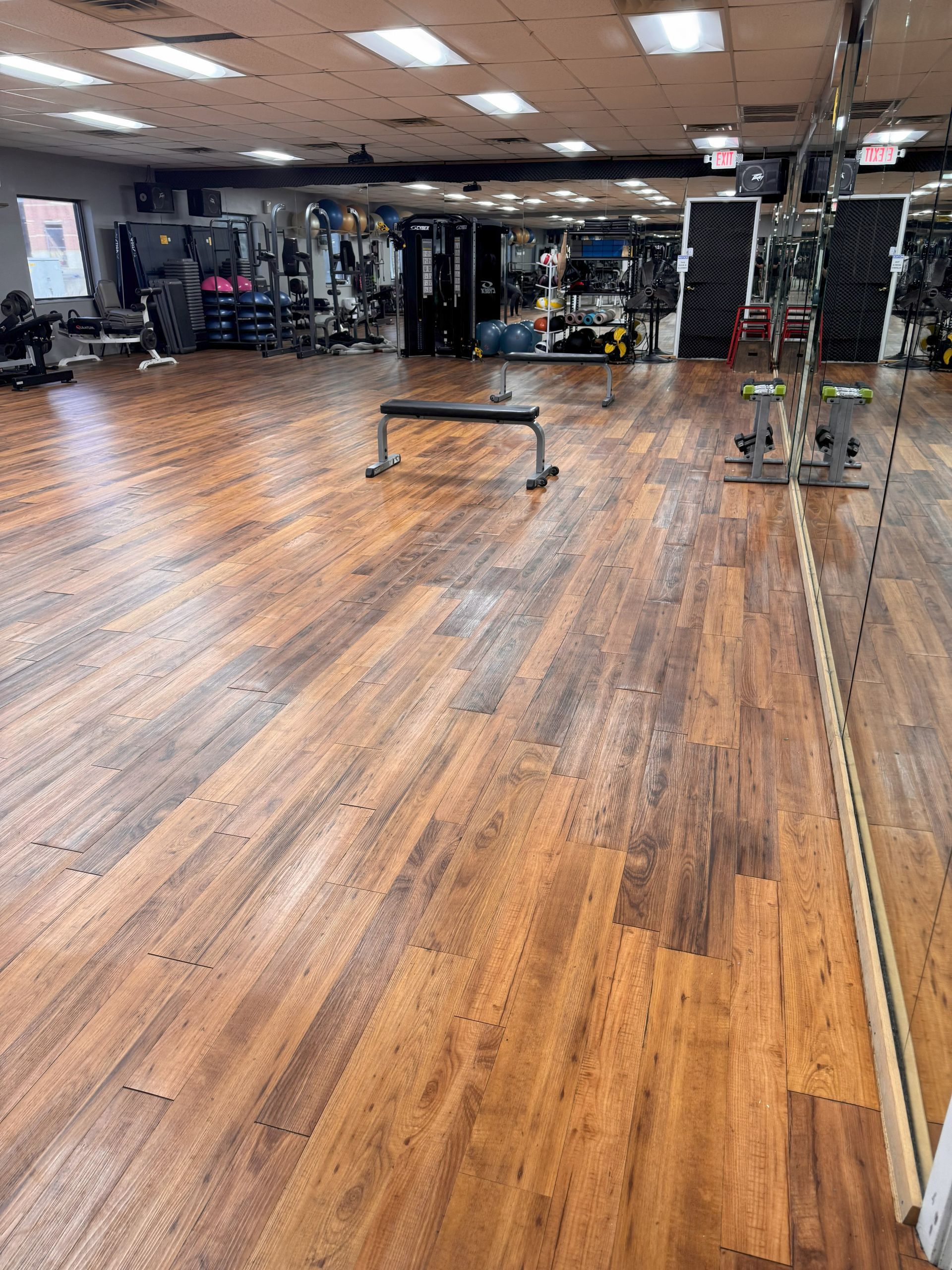 A large empty gym with wooden floors and a mirror