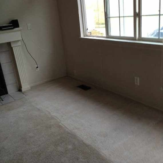 Empty carpeted room with fireplace, window, and wall vent