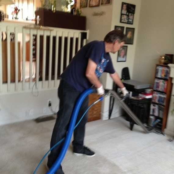 Person vacuuming a carpet in a living room with a blue hose