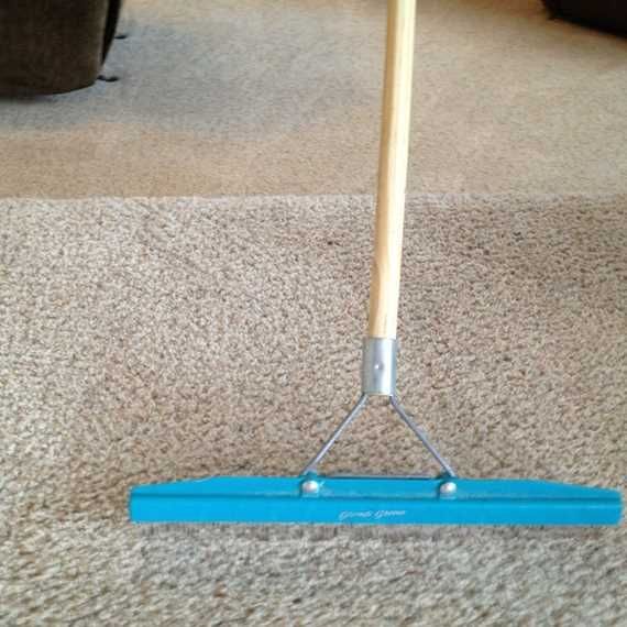 Blue floor squeegee with wooden handle on beige carpet