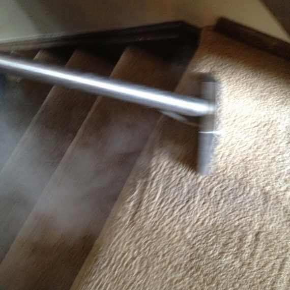 Metal handrail beside wooden stairs and beige carpeted landing