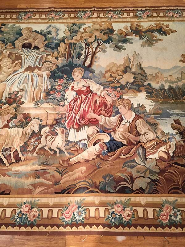 Tapestry rug with a pastoral scene of a couple, animals, and nature, framed by a floral border.