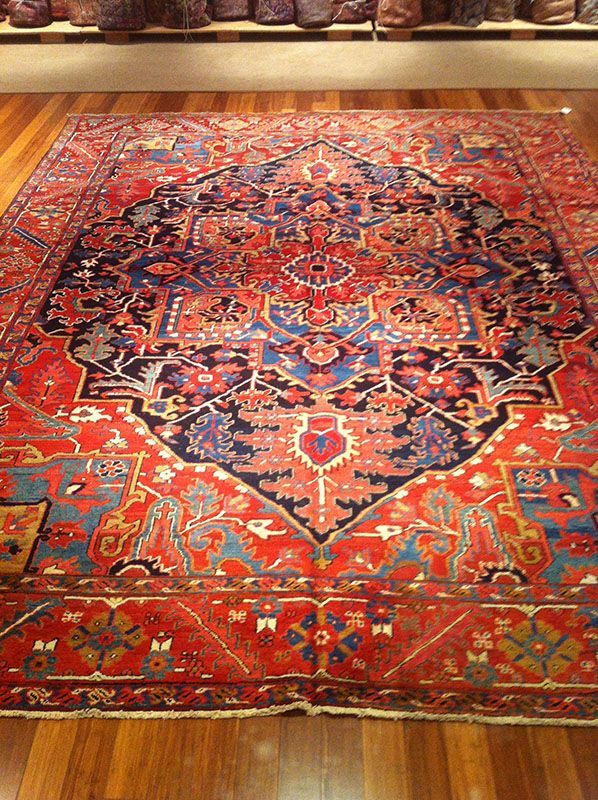 Red and blue Persian rug with intricate floral and geometric patterns on wood floor.