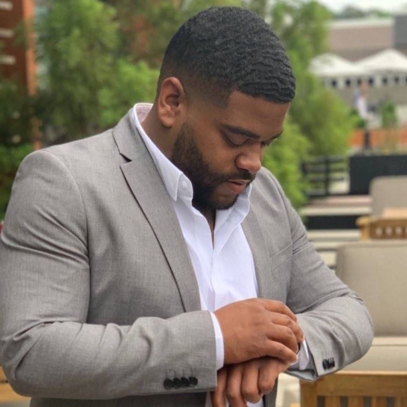 Man in grey suit checks his watch outdoors.