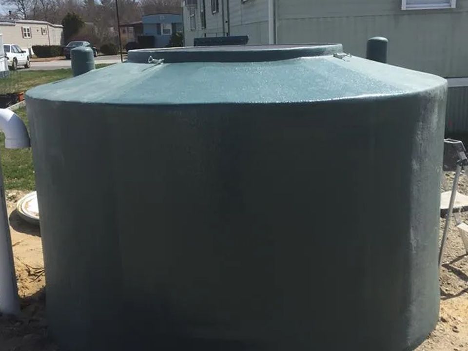A large gray tank is sitting in the dirt in front of a house.