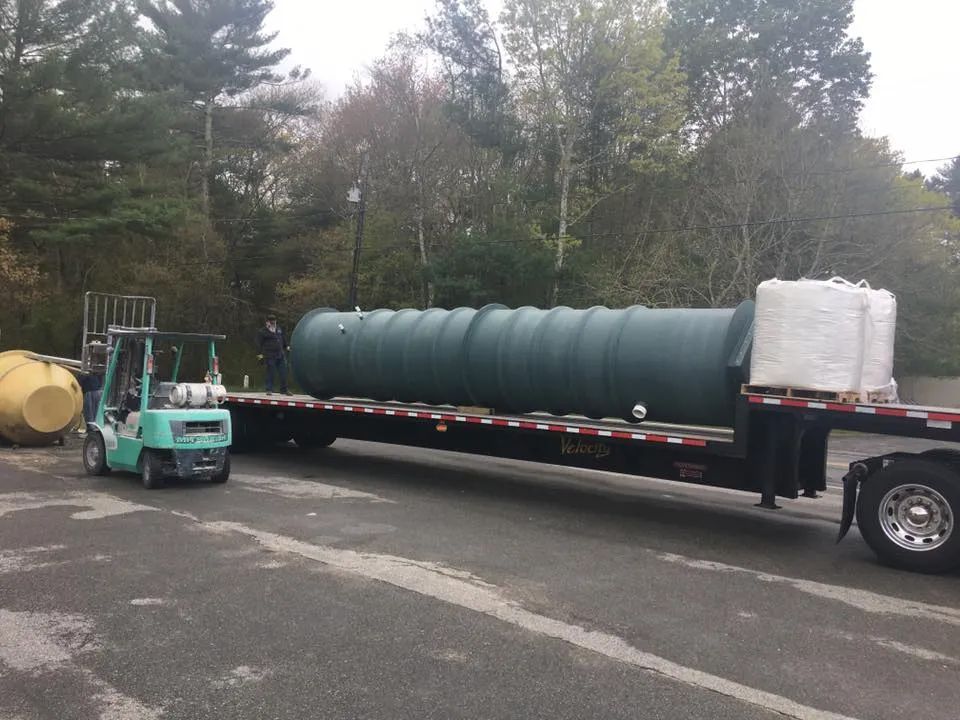 A forklift is pulling a large green tank on a trailer.