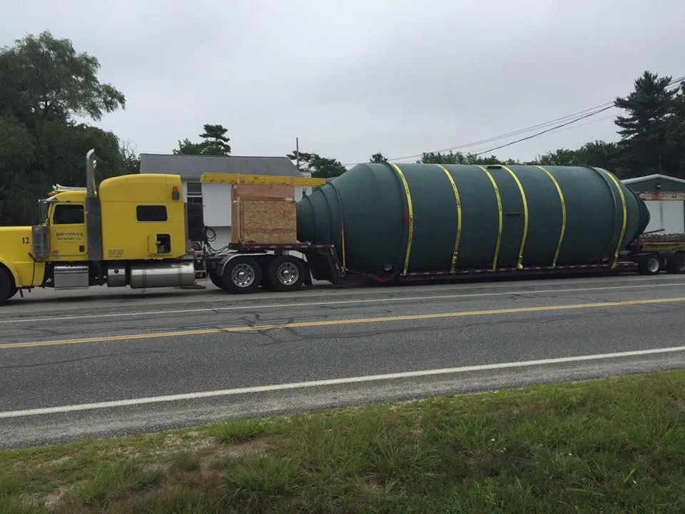 A yellow semi truck is carrying a large green object down a road.