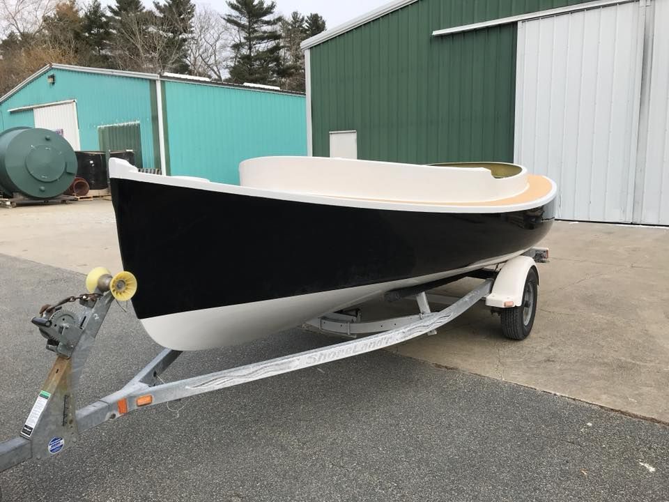 A small boat is on a trailer in front of a green building.