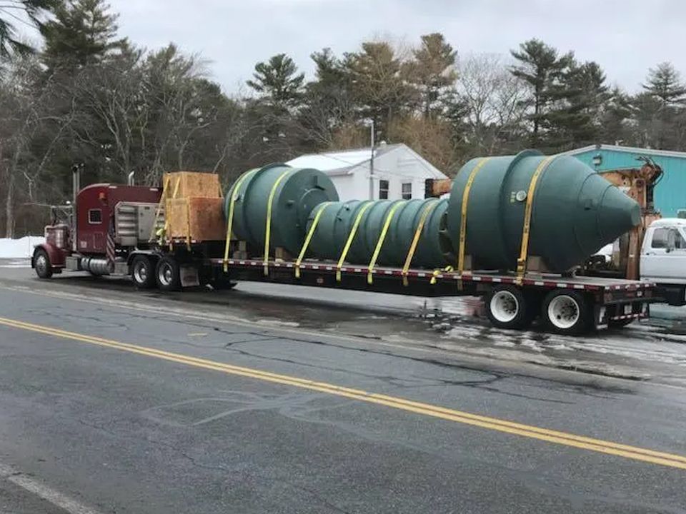 A semi truck is carrying a large green object on a flatbed trailer.