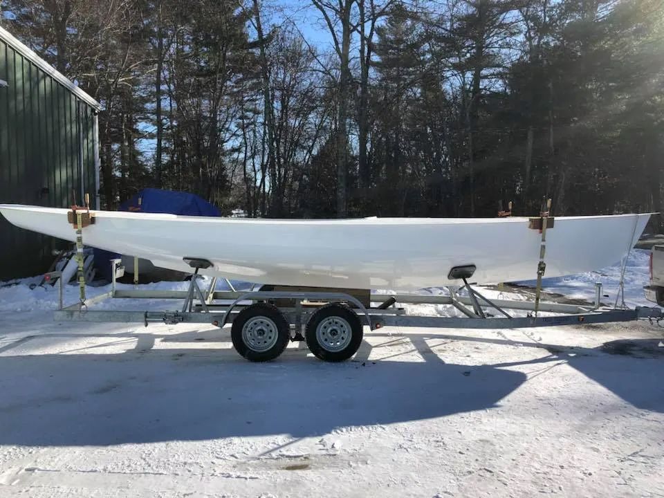 A white boat is on a trailer in the snow.