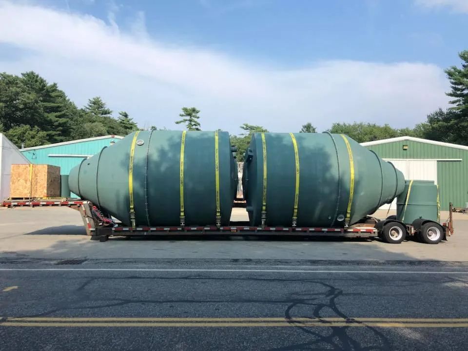 A large green tank is on a trailer on the side of the road.