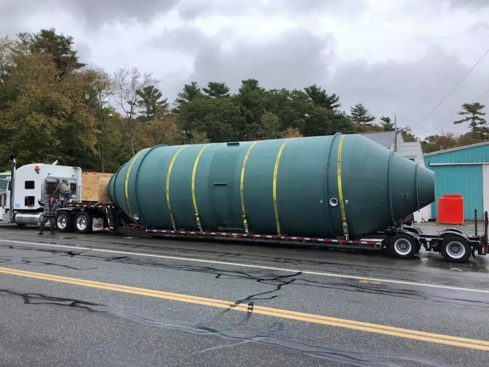 A large green tank is being transported on a trailer down a road.