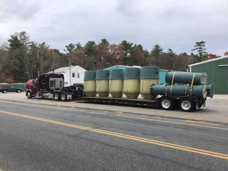 A semi truck is pulling a trailer full of tanks down a road.