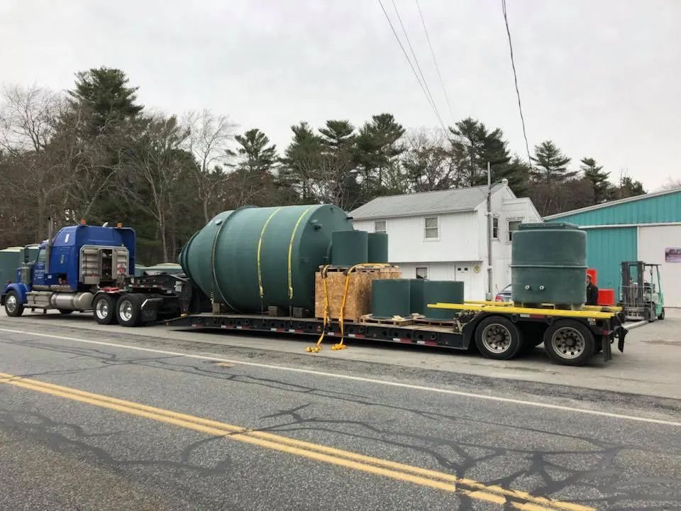 A semi truck is carrying a large green tank down a road.
