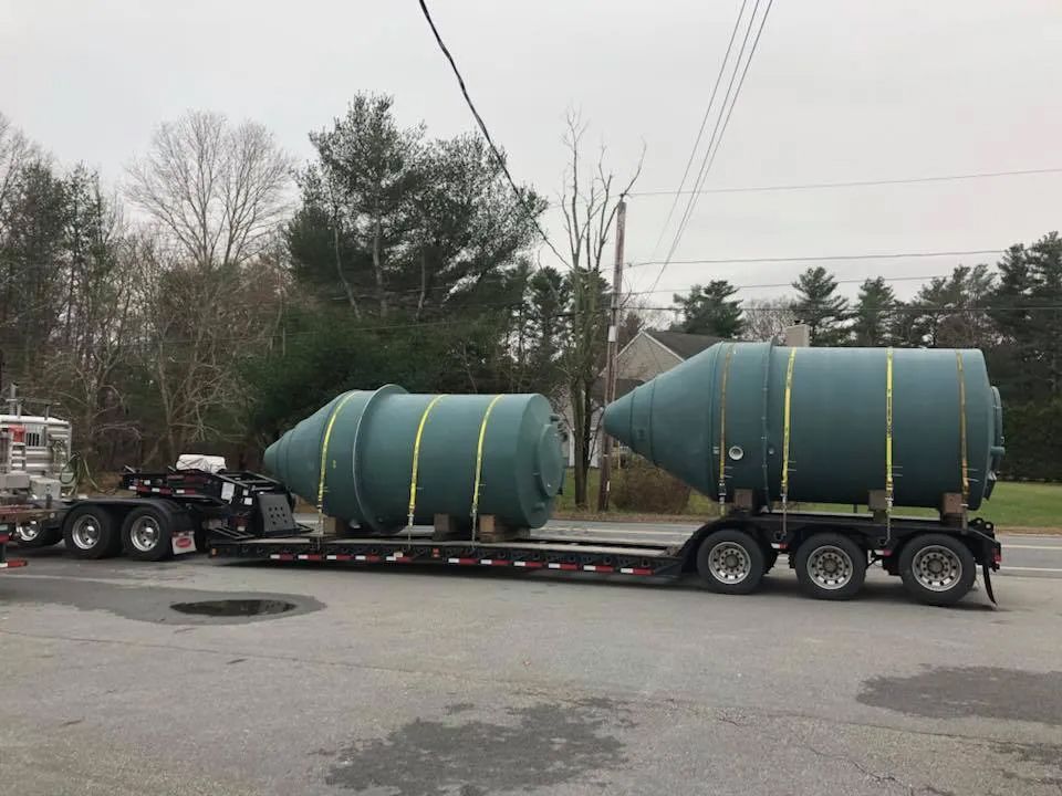 A semi truck is carrying two large green tanks on a trailer.
