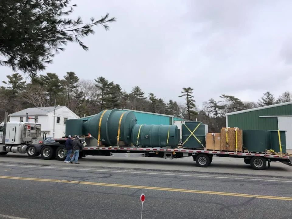 A semi truck is carrying a large green tank on a flatbed trailer.