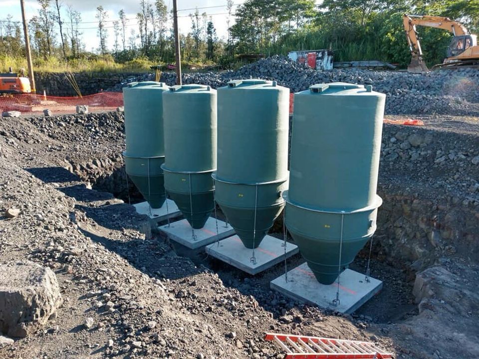 A row of green silos are sitting in a pile of dirt.
