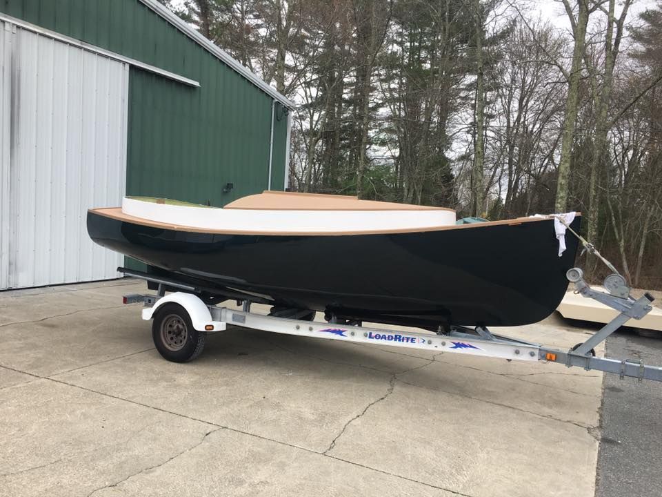 A black boat is on a trailer in front of a green building.