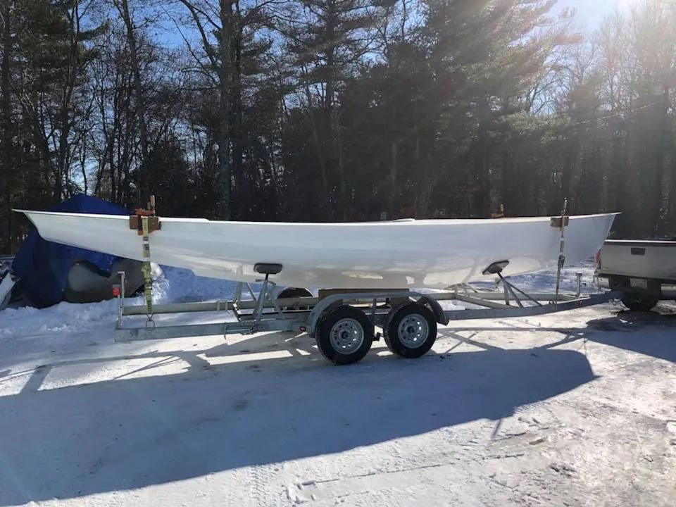 A white boat is on a trailer in the snow.