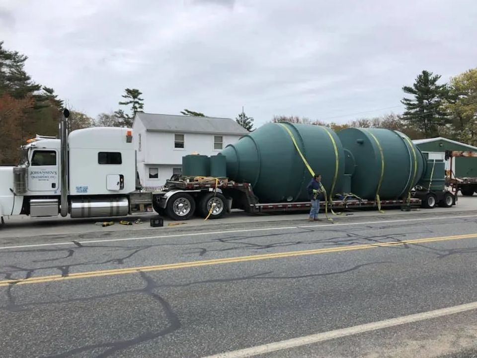 A semi truck is carrying a large green object down a road.