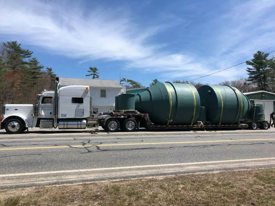 A semi truck is carrying a large green tank down a road.