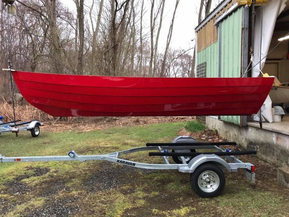 A red boat is on a trailer in front of a building.