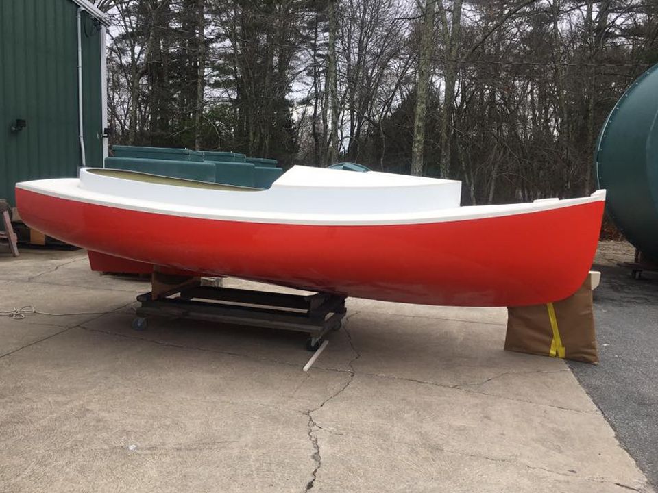 A red and white boat is sitting on the side of the road.