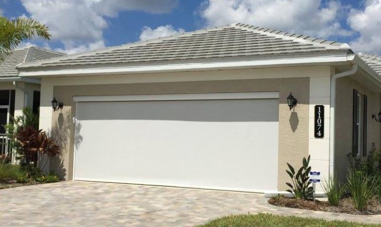 White garage door with retractable shade on a beige house under a blue sky.