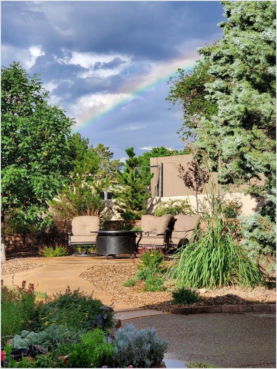 Rainbow over a garden with a fountain, seating area, and lush greenery.